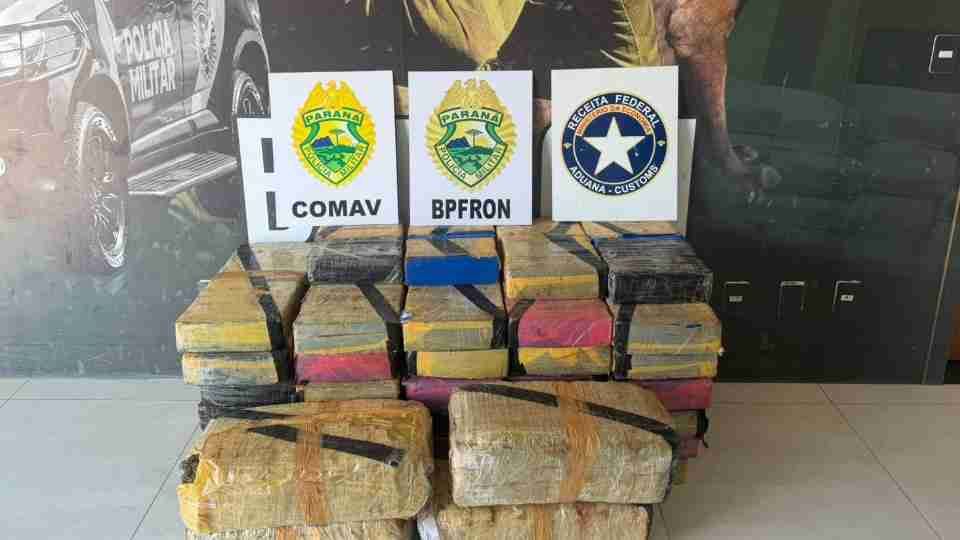 Tabletes de maconha apreendidos e dispostos sobre um veículo, com agentes policiais ao fundo.