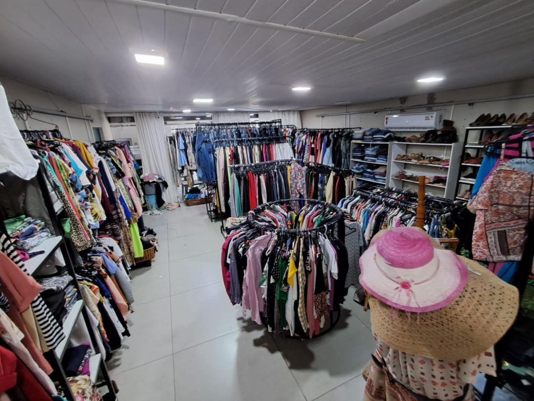 Araras repletas de roupas organizadas no interior do Bazar Refúgio em Toledo