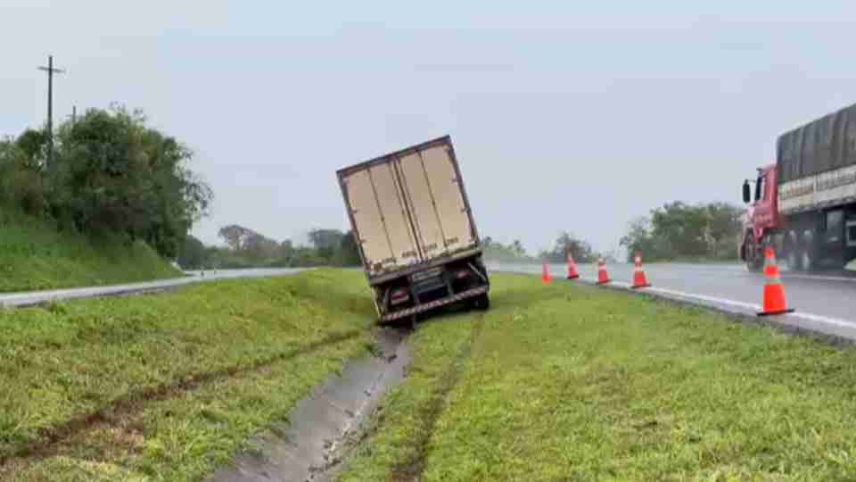Caminhão-baú imobilizado dentro da canaleta de escoamento entre as pistas da BR-163, próximo a Toledo, durante um dia chuvoso.