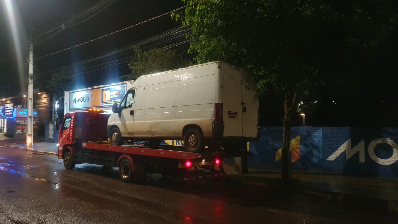 Furgão branco sendo transportado em plataforma de caminhão-guincho em via urbana de Toledo