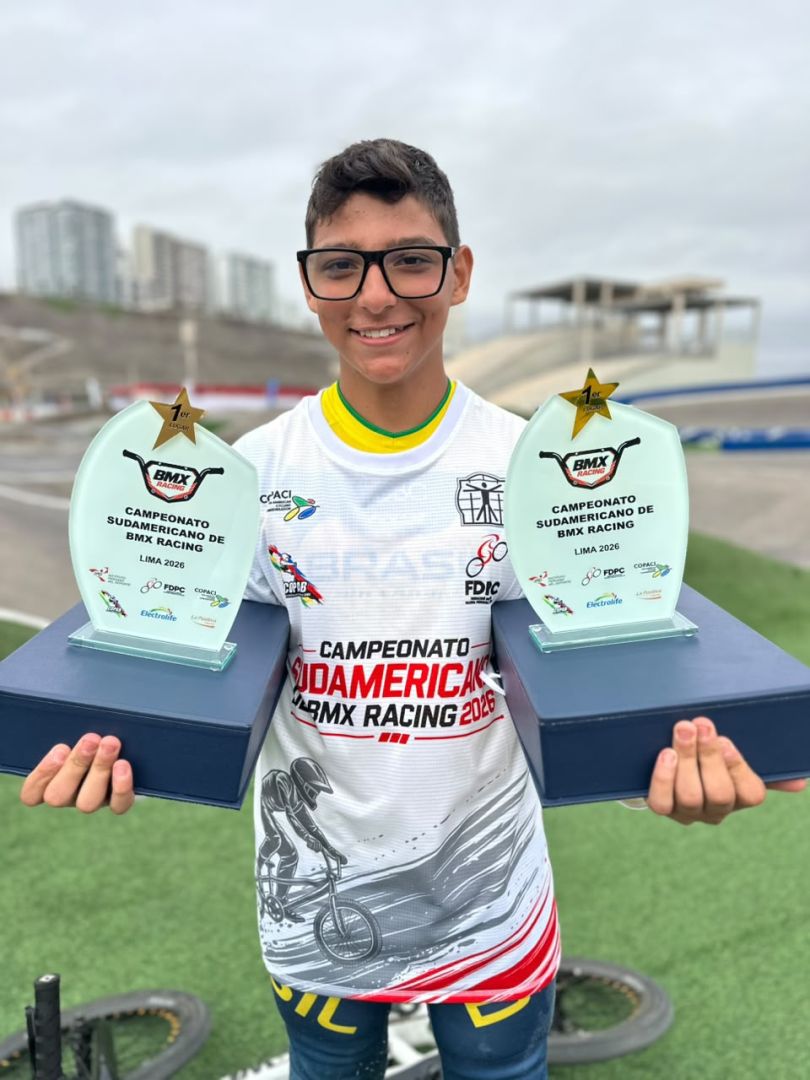 Jovem atleta Heitor Isaque comemorando vitória em competição de BMX Racing no Peru, segurando troféus.