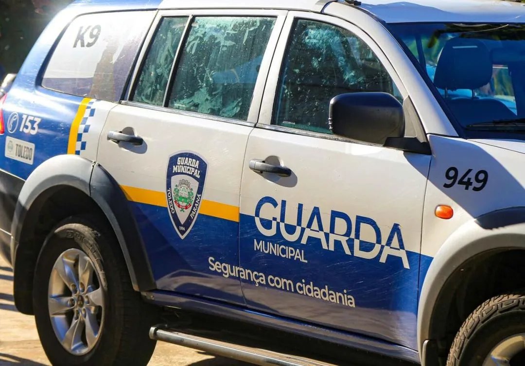 Fachada da 20ª Subdivisão Policial de Toledo com viaturas da Guarda Municipal estacionadas em frente.