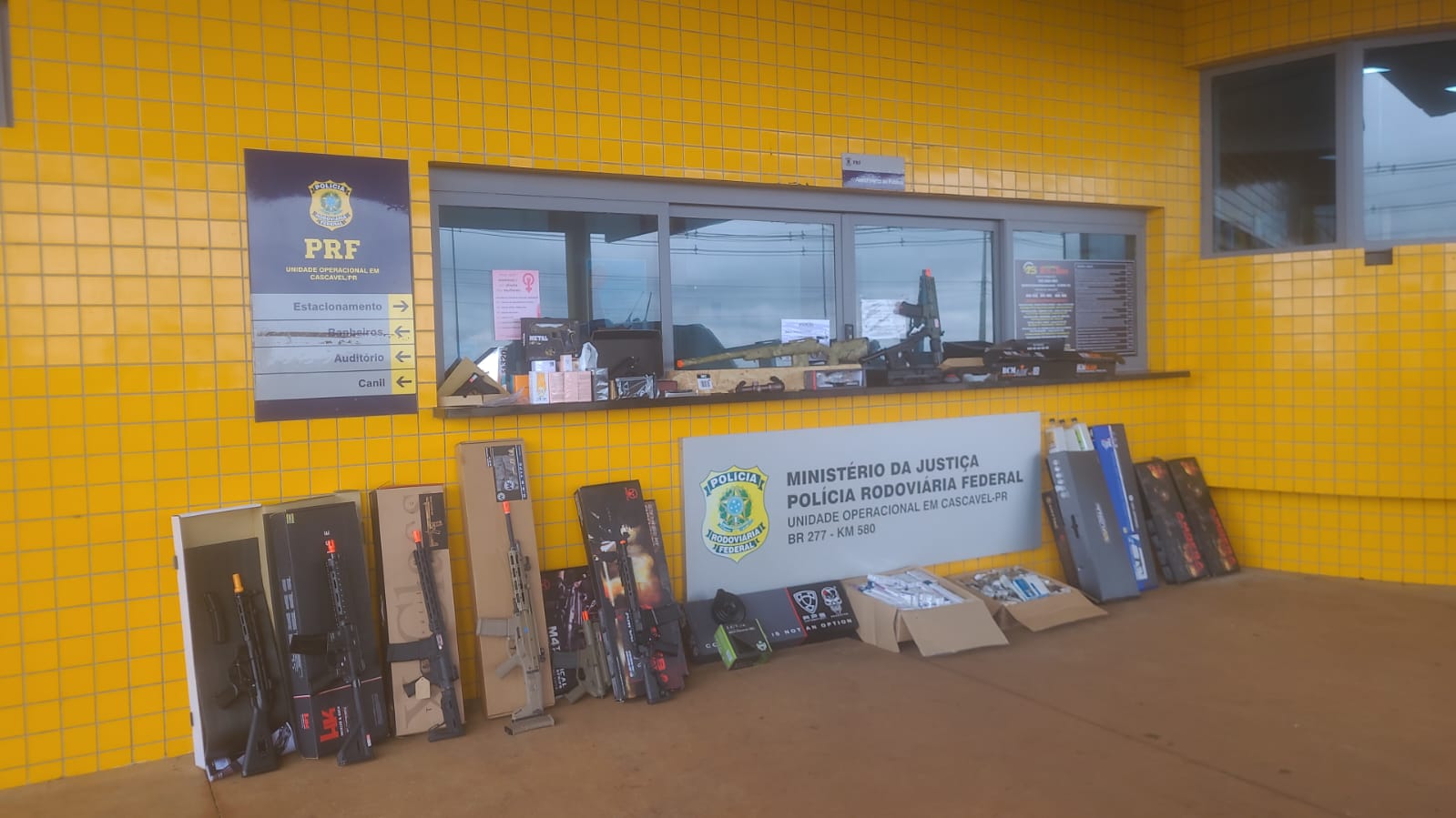 Agentes da Polícia Rodoviária Federal organizam mercadorias apreendidas, incluindo armas de airsoft e medicamentos, sobre uma mesa durante fiscalização na BR-277