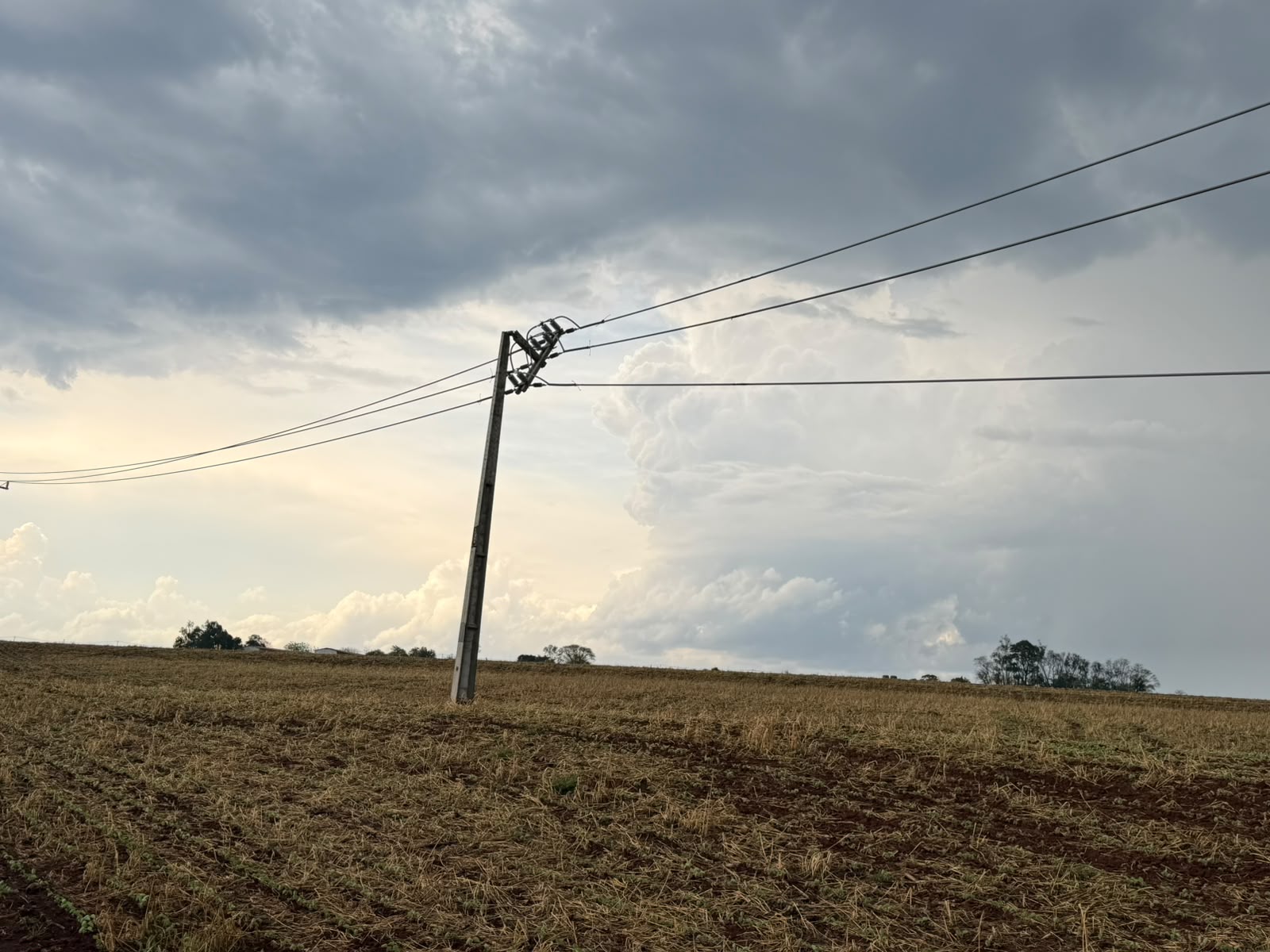 Poste de energia elétrica caído em área urbana com fiação espalhada pela via pública após forte temporal.